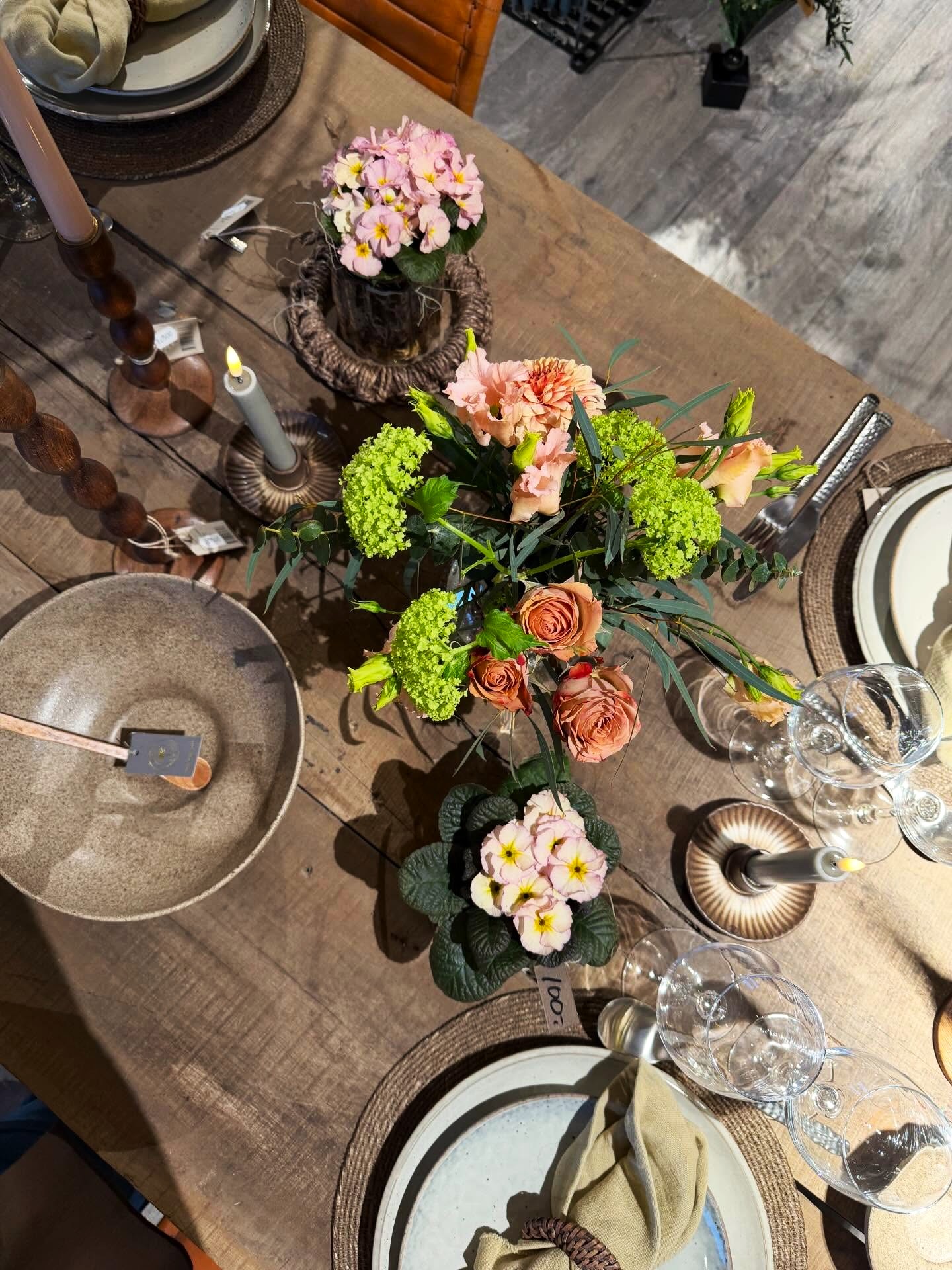 Bord dækket med cremefarvet service og en buket af snitblomster i vase. 