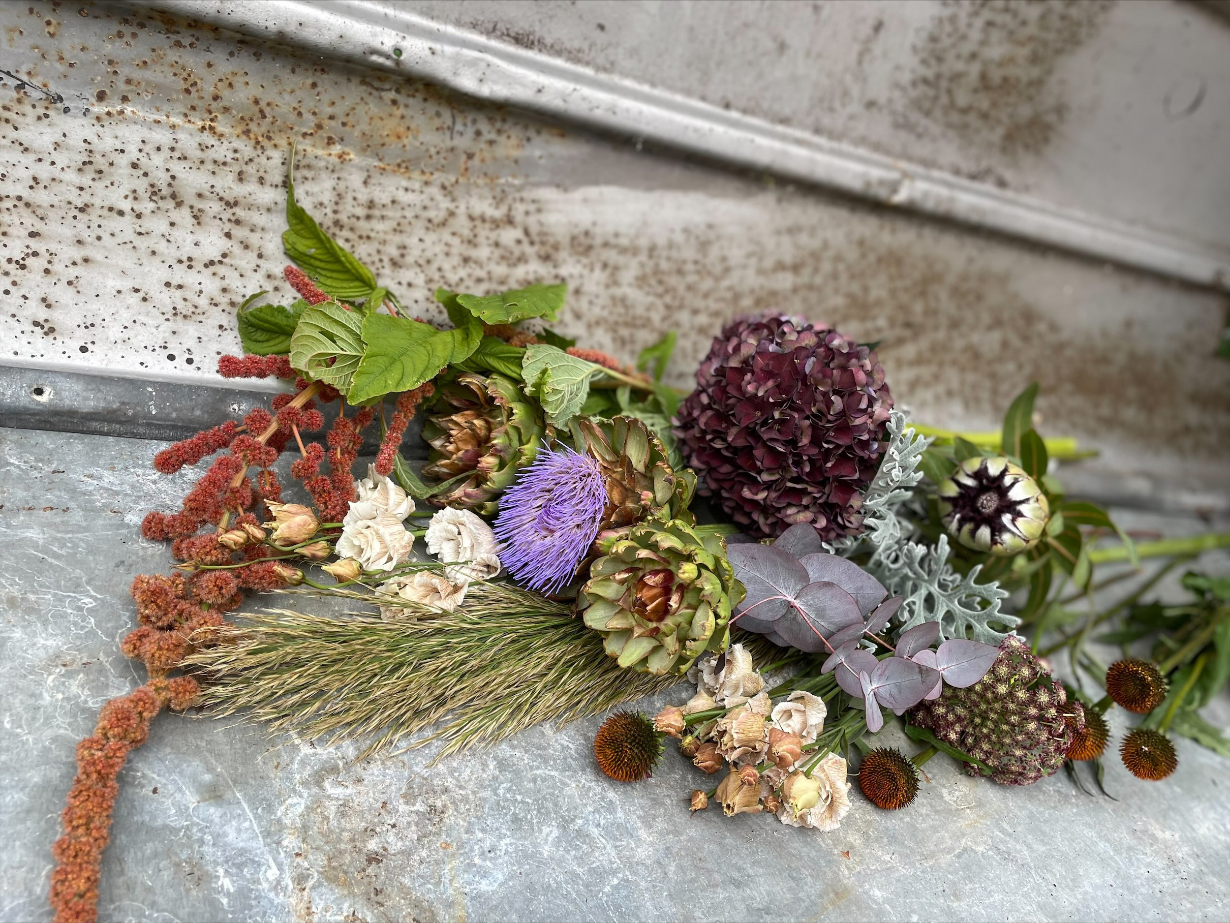 Afskårne blomster og dekorationsmaterialer ligger på patineret zinkbord