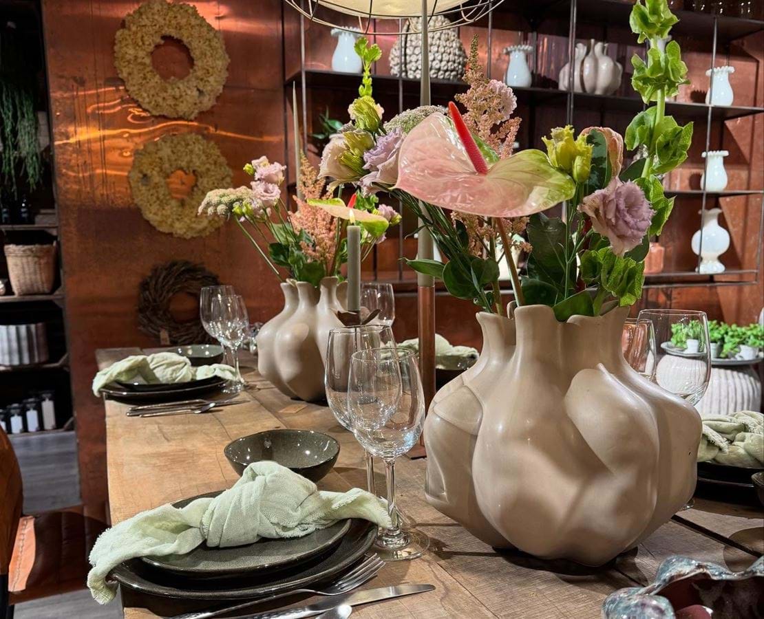 Blomsterbutikken Flora Flora med et opdækket plankebord af cremefarvet vase med afskårne blomster og smukt service.