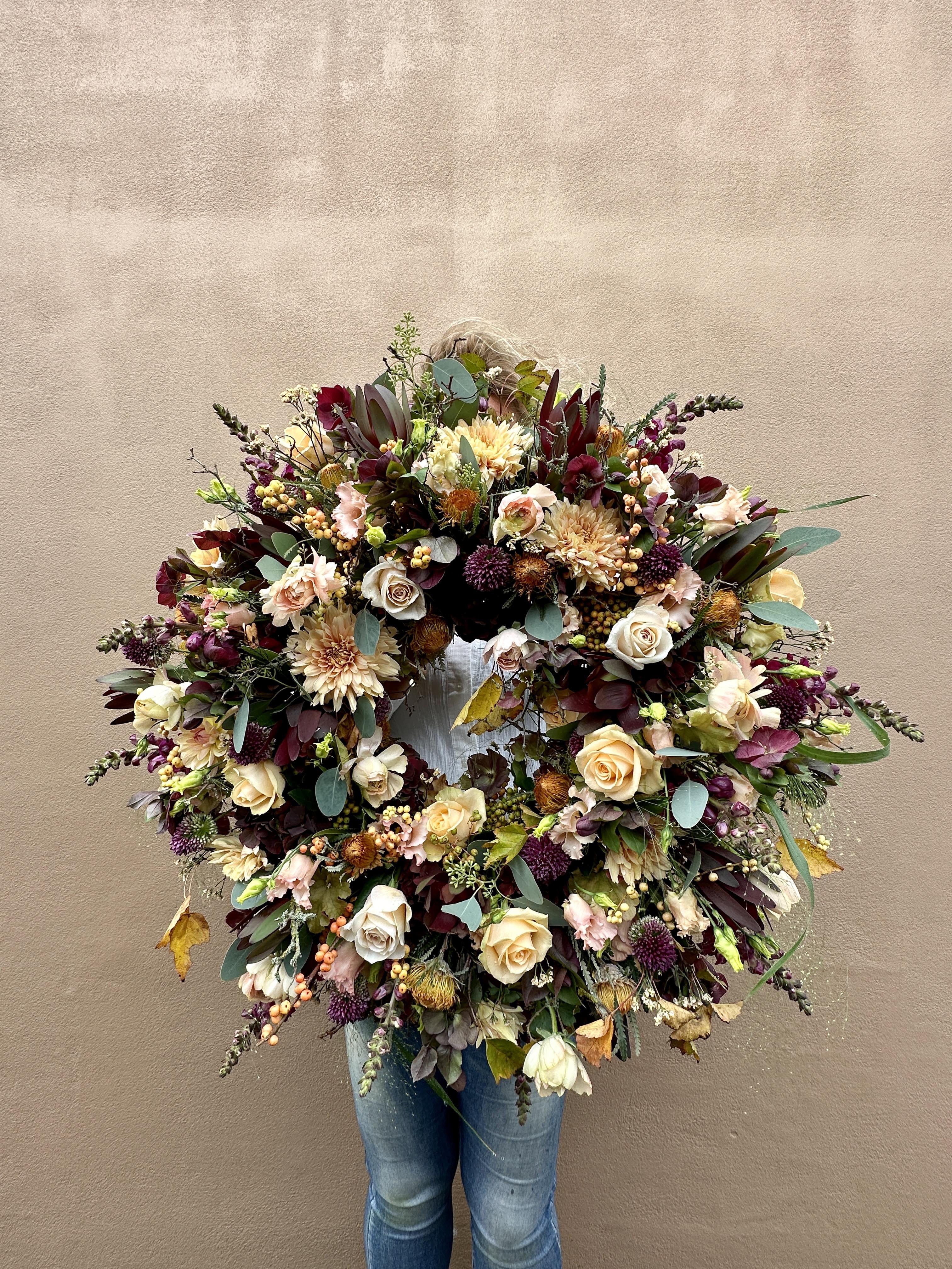 Stor begravelseskrans bundet med blomster i creme, lilla og bordeaux nuancer.