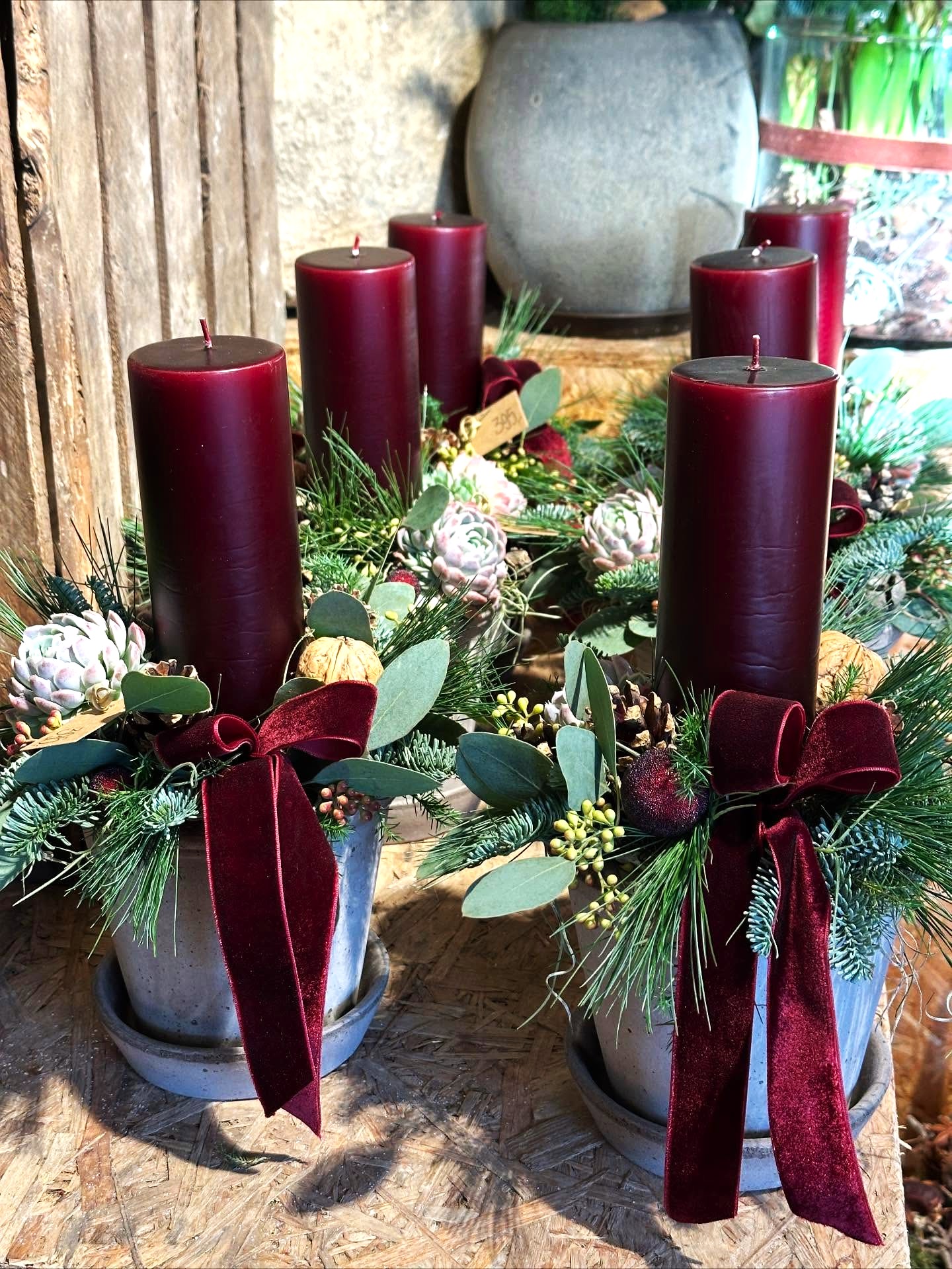 Juledekorationer i Bergs potter står pyntet med gran, rød sløjfe og i midten et rødt bloklys. 