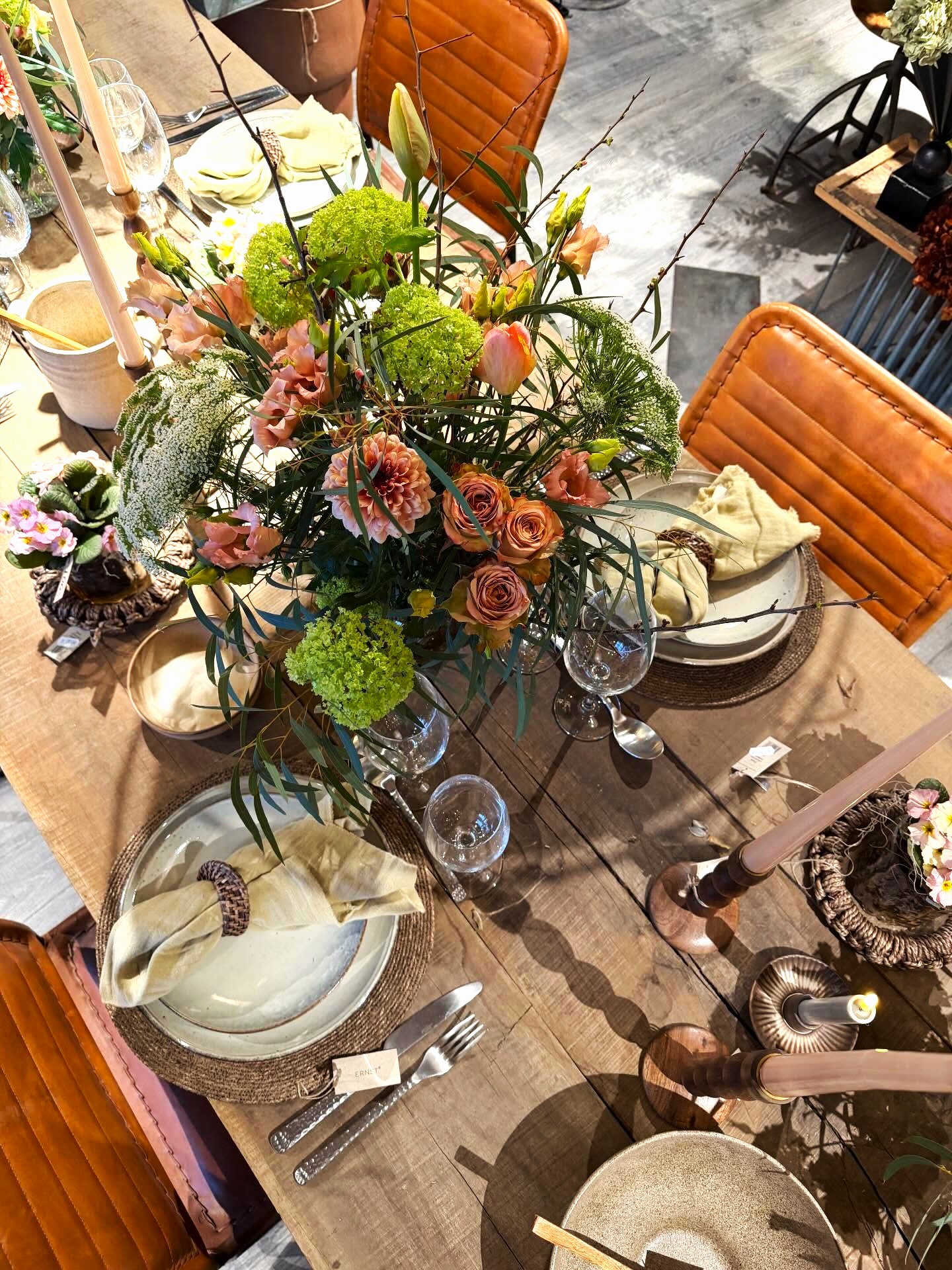 Plankebord pyntet med en fyldig buket blomster og dækket med råhvidt service på flettede dækservietter. 