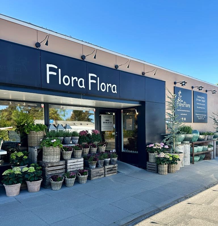 Facaden af butikken Flora Flora, sat op med planter, krukker, kurve og træer i forskellige afskygninger.