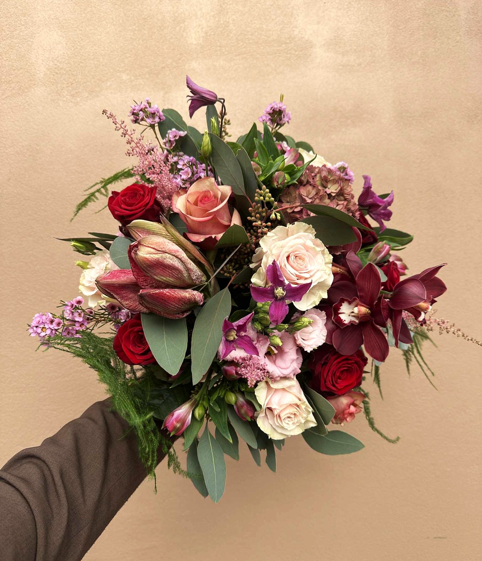 Buket bundet med røde roser, amaryllis, cremefarvede blomster og lilla blomster. 