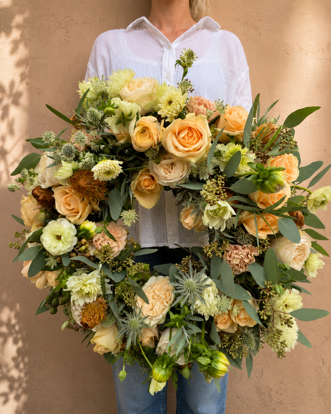 Stor begravelseskrans bundet med blomster i creme, lyse og varme nuancer.