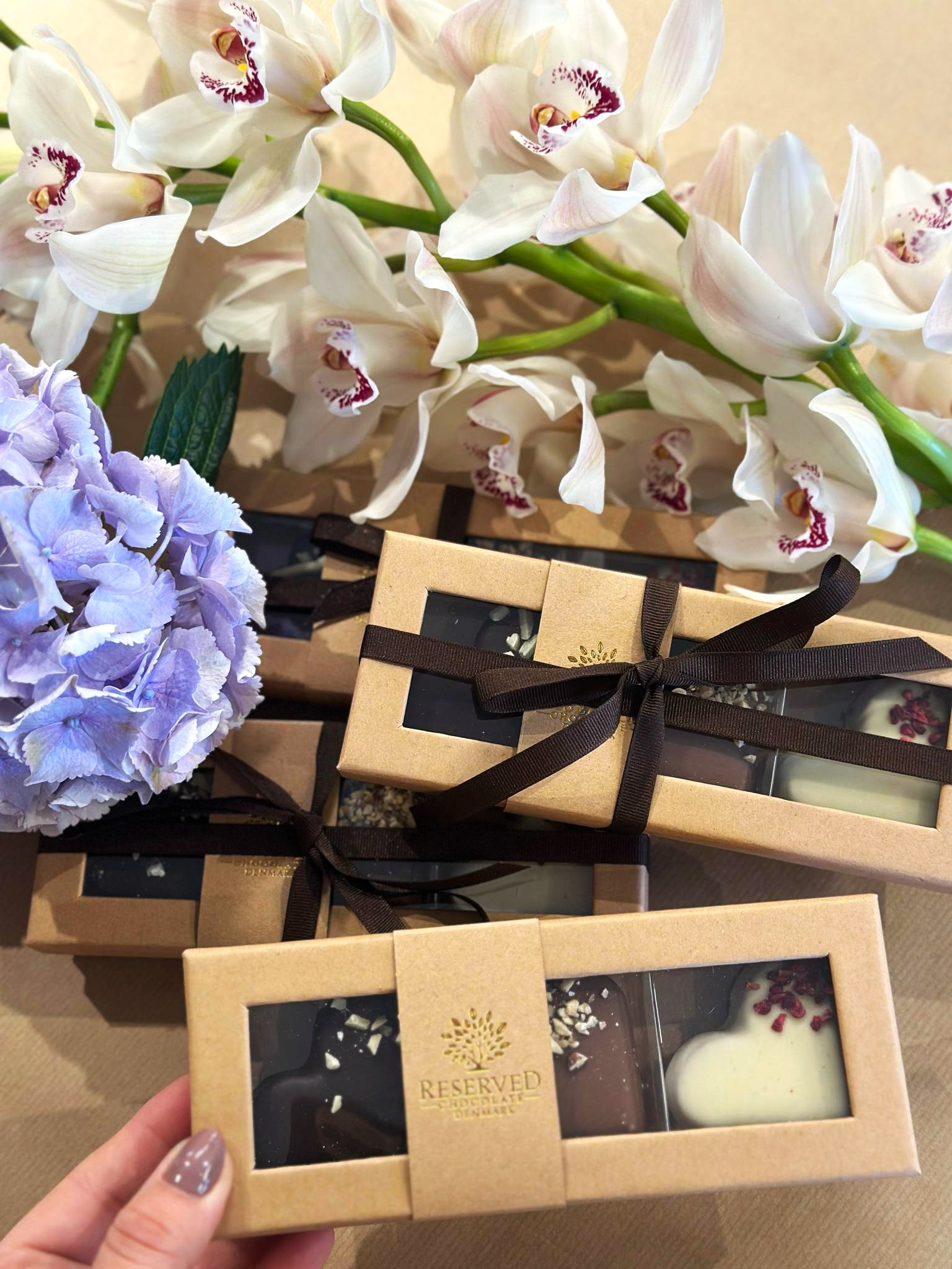 Marcipanhjerte i hvid, lys og mørk chokolade ligger i aflange papiræsker. 