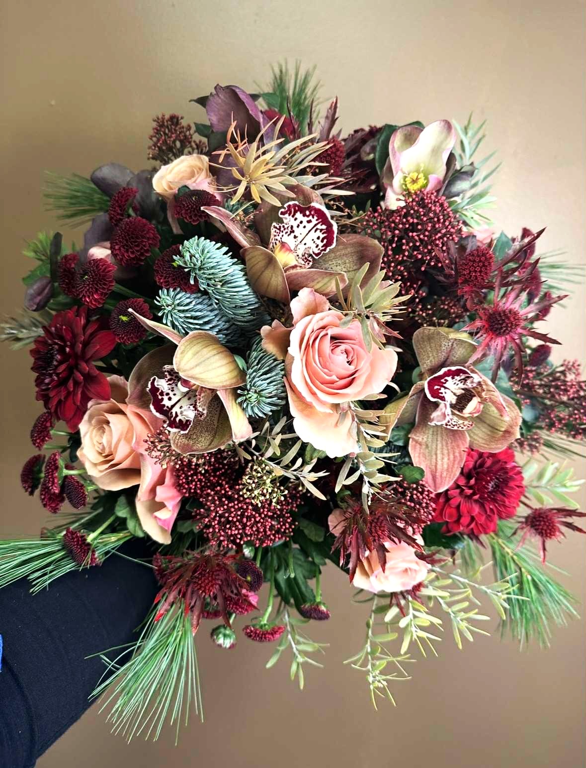 Tæt julebuket fyldt med blomster i julerøde, lilla, bourdeax, lyserøde farver. Den er bundet med gran og blandet vintergrønt. 